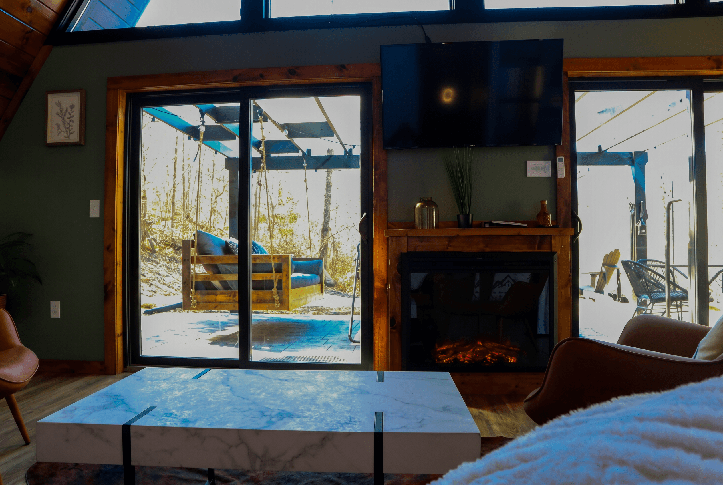 A-frame living room with an electric fireplace, a marble coffee table and glass doors to a deck with a hanging bed swing