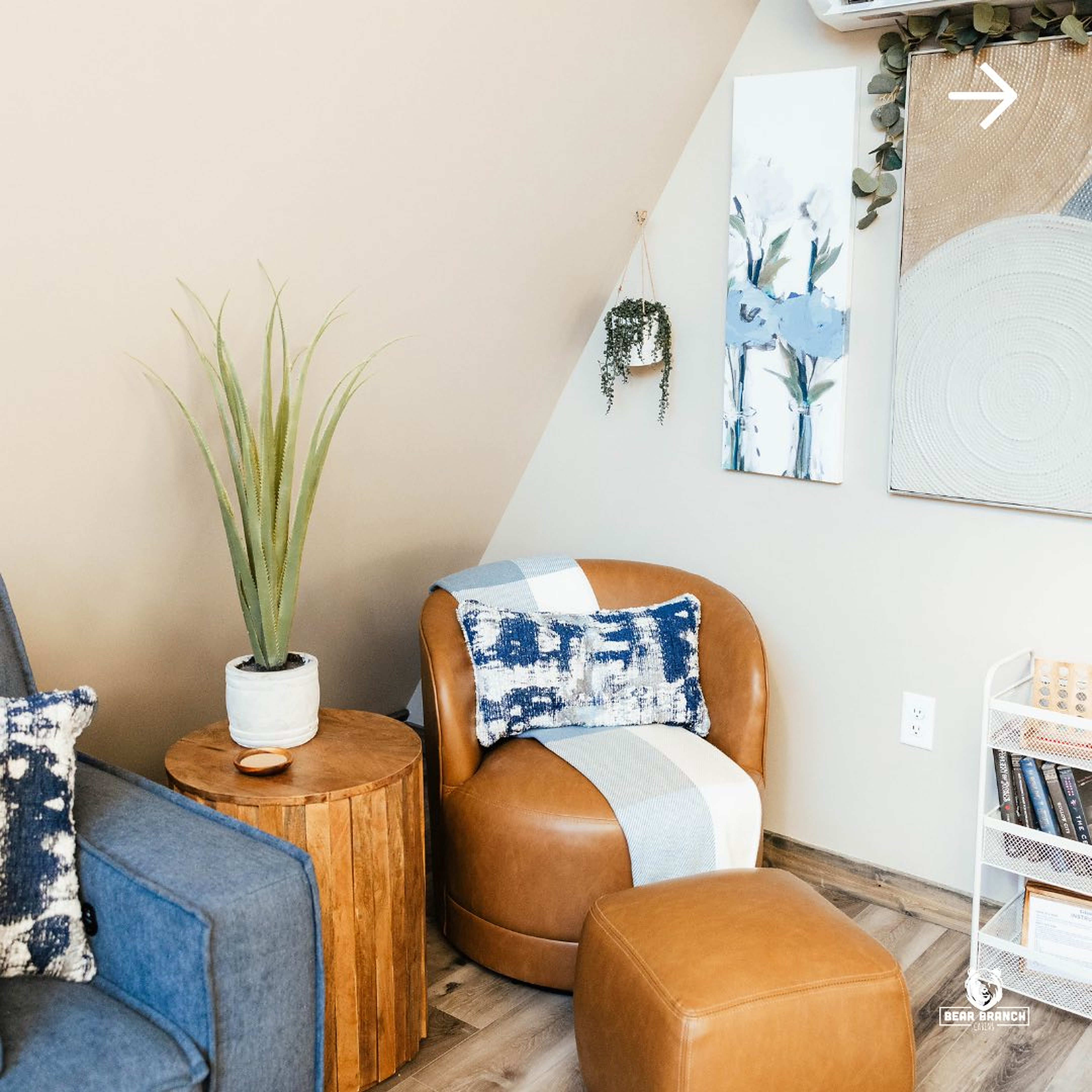 Cabin seating corner with a tan leather swivel chair and ottoman, a wooden side table and blue patterned pillows