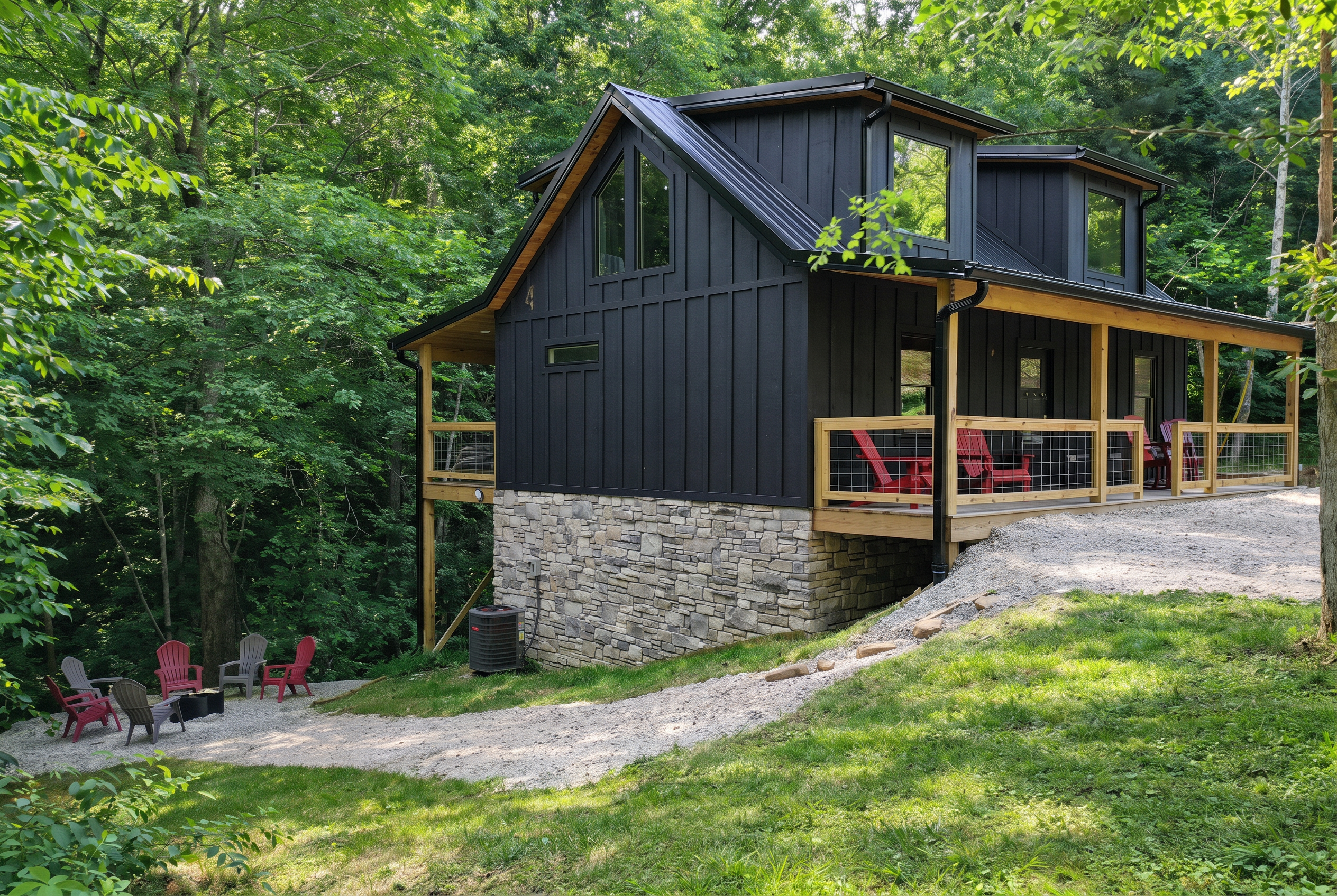Black board-and-batten cabin on a stone base with a covered porch, red chairs and a fire pit in the woods