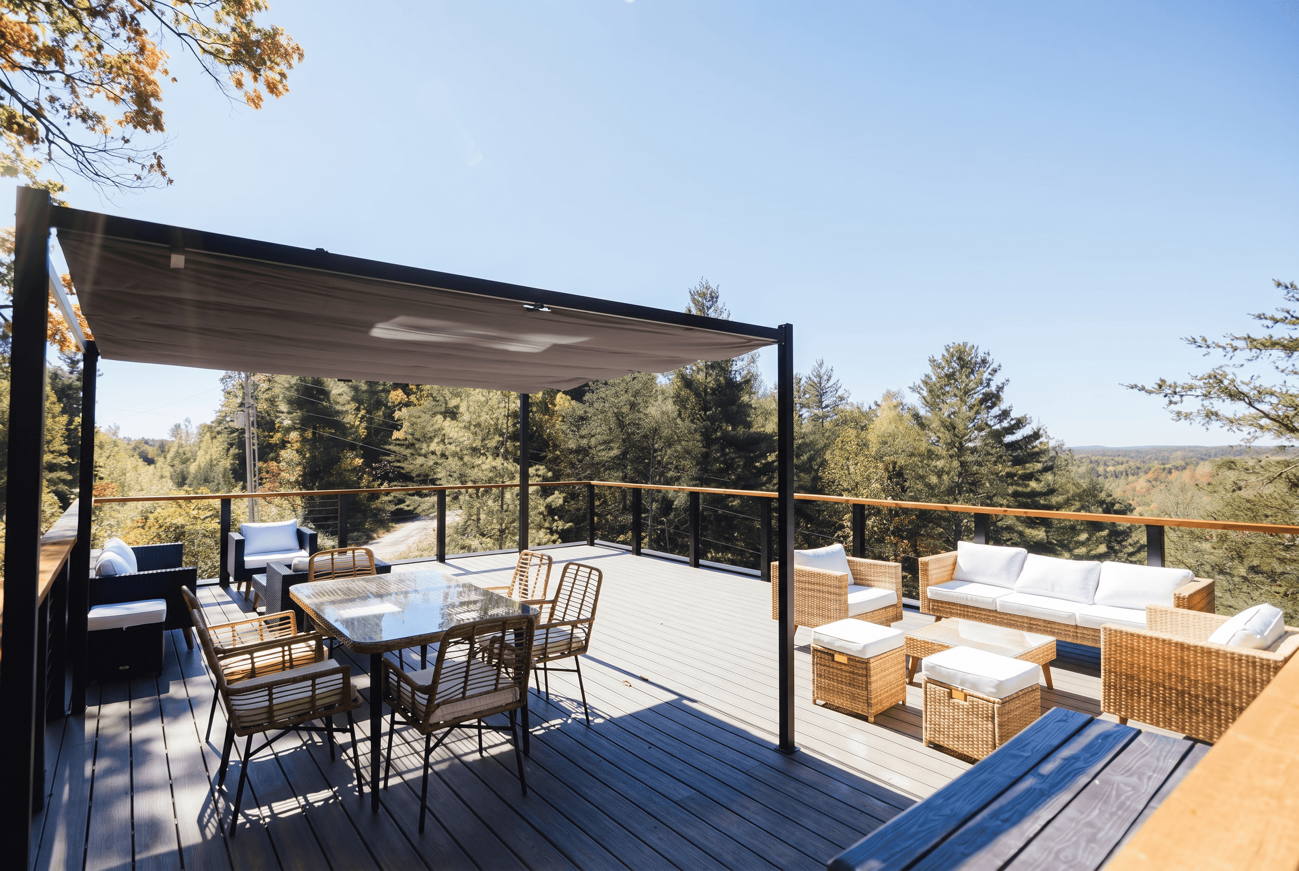 Rooftop deck with a shade canopy, an outdoor dining table and wicker sofas overlooking a forested valley