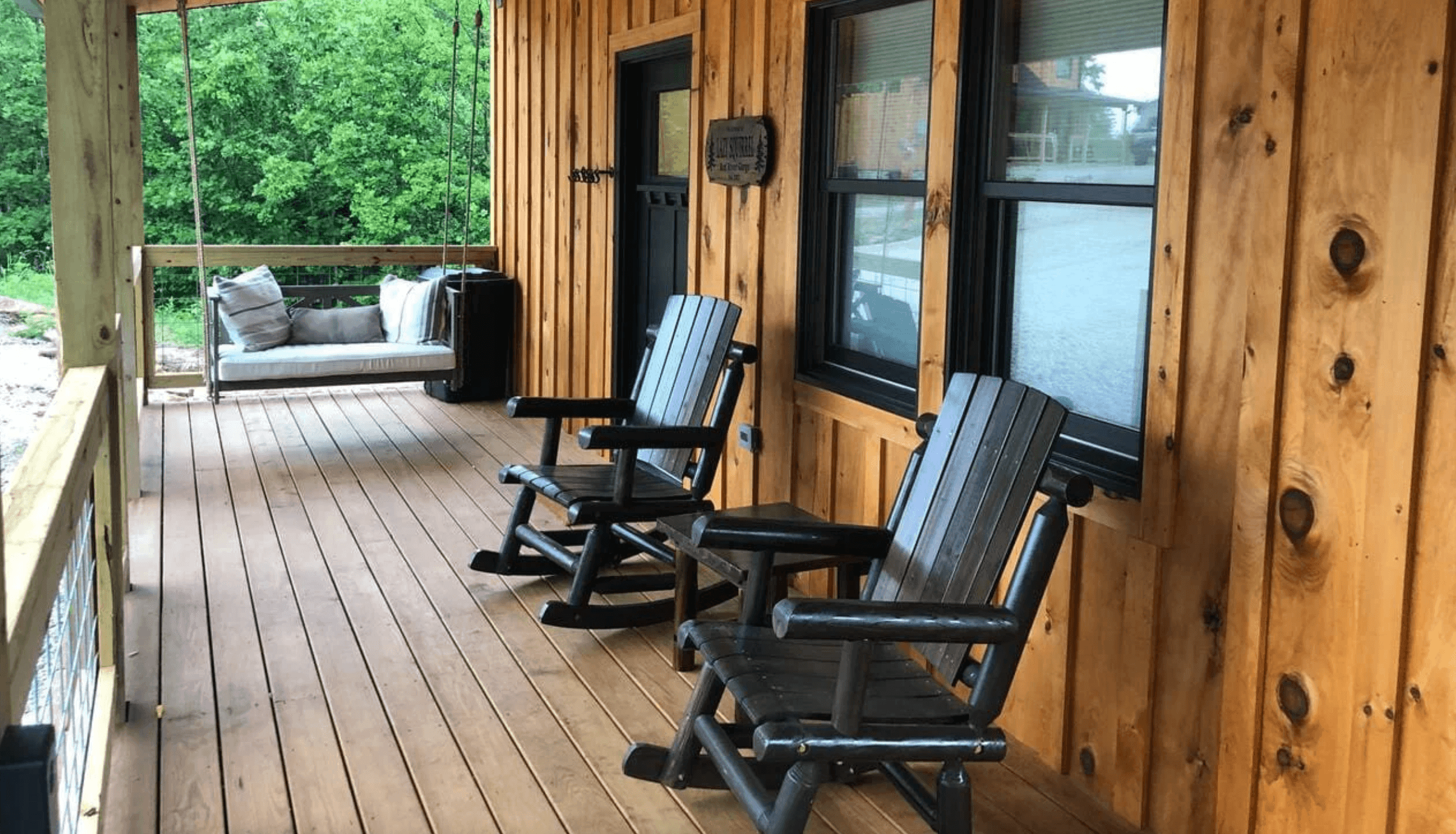 Covered cabin porch with log rocking chairs and a porch swing along a knotty pine wall