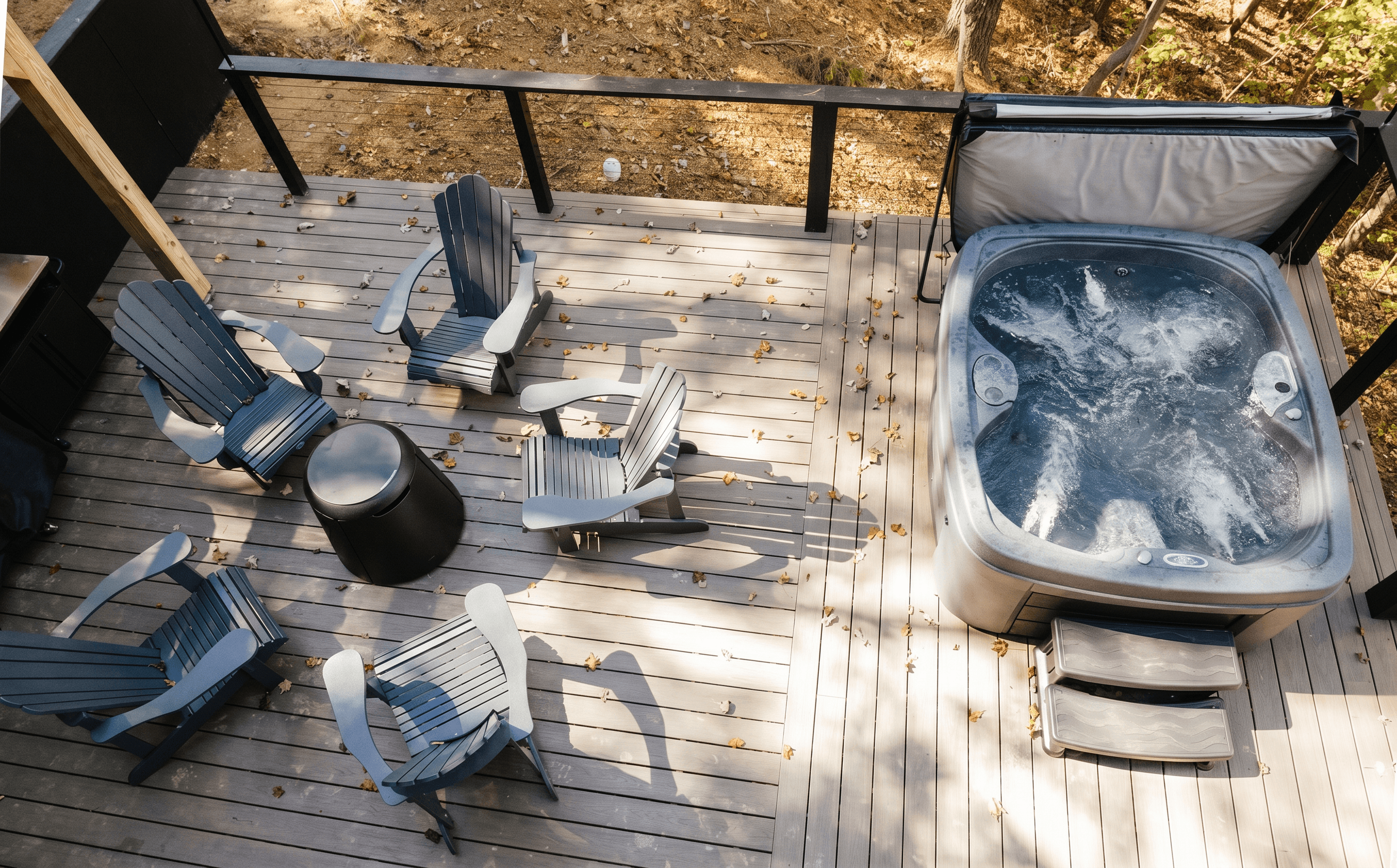 Deck seen from above with Adirondack chairs around a fire table next to a bubbling hot tub