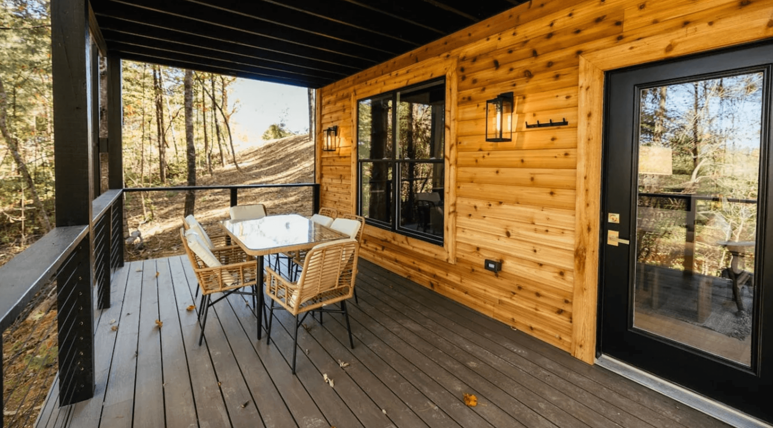 Covered cabin porch with wicker dining chairs around a glass table beside cedar plank walls